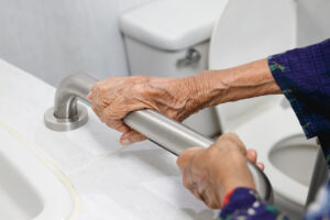 Mano di una persona anziana che si aggrappa a una delle maniglie di sicurezza, uno degli ausili bagno anziani, accanto al WC.
