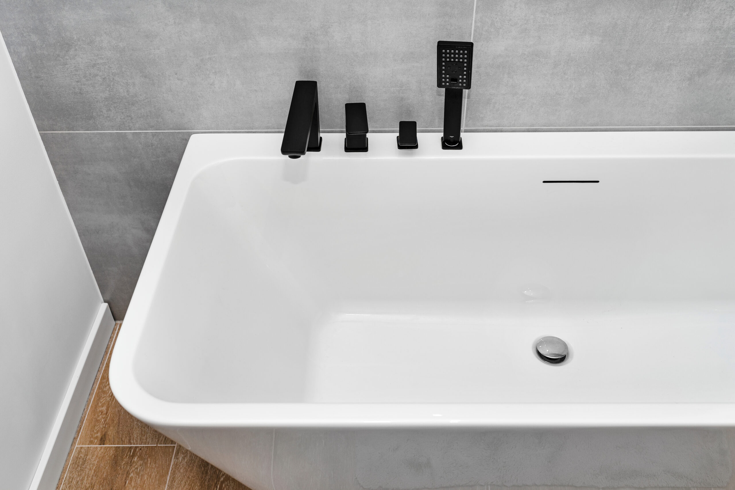 Una moderna vasca da bagno bianca con rubinetteria nera, posizionata accanto a eleganti piastrelle grigie, illustra come cambiare la vasca senza danneggiare le piastrelle circostanti.