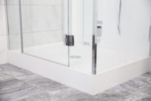 Un piatto doccia bianco ergonomico, incassato nel pavimento, con una porta in vetro trasparente e maniglie in metallo nero, rappresenta una soluzione moderna e minimalista per un bagno funzionale.