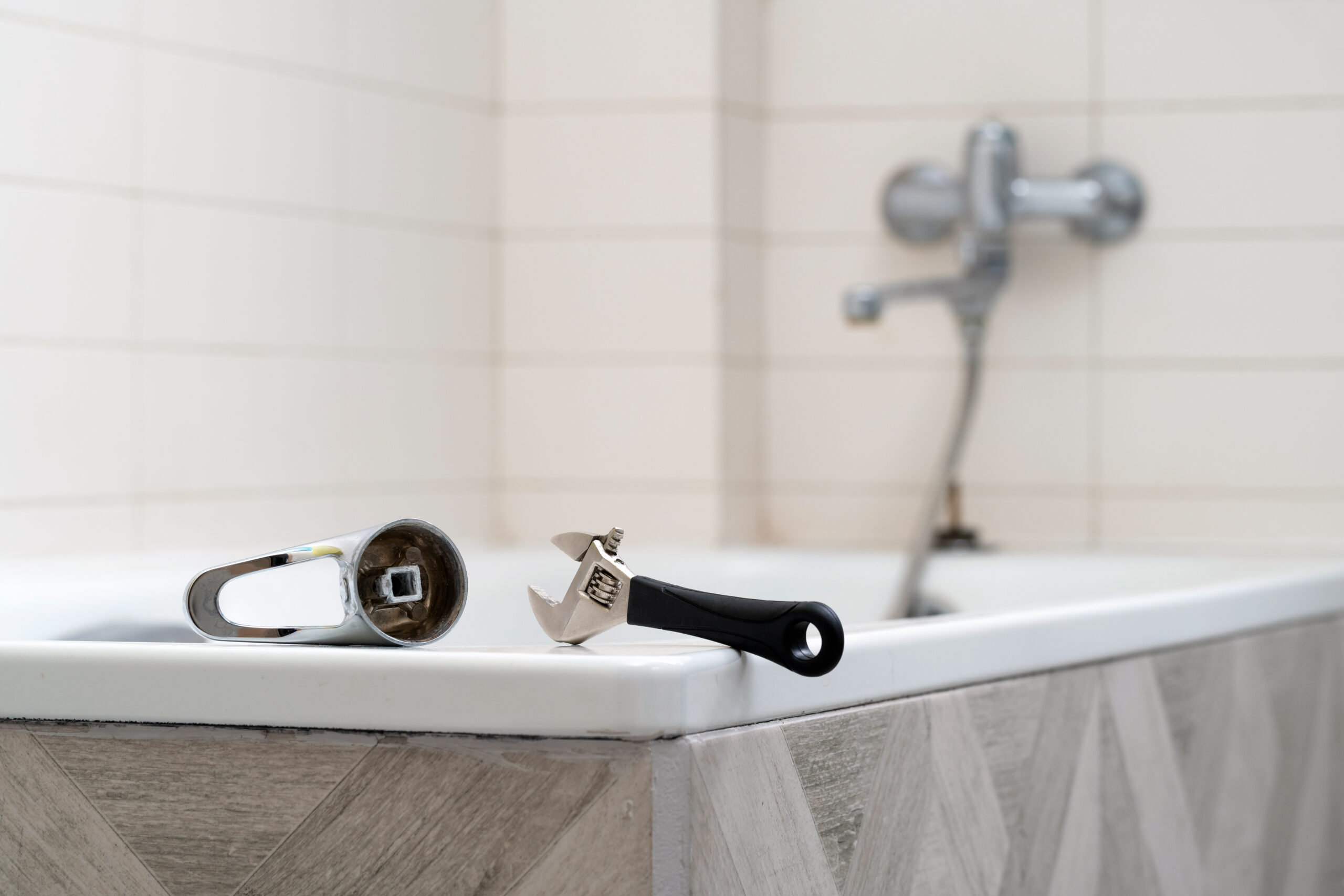 Una chiave inglese e un taglierino posizionati sul bordo di una vasca da bagno, simboleggiano l'inizio della sostituzione della vasca con Tecnobad, esperti nella trasformazione del tuo bagno.