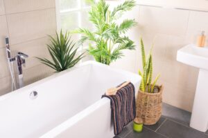 Una vasca da bagno bianca e lussuosa, accanto a piante verdi in un bagno moderno con piastrelle neutre, simbolizza un rinnovamento attraverso la sovrapposizione vasca da bagno. Questa tecnica offre un restyling fresco e moderno, mantenendo intatto il design esistente.