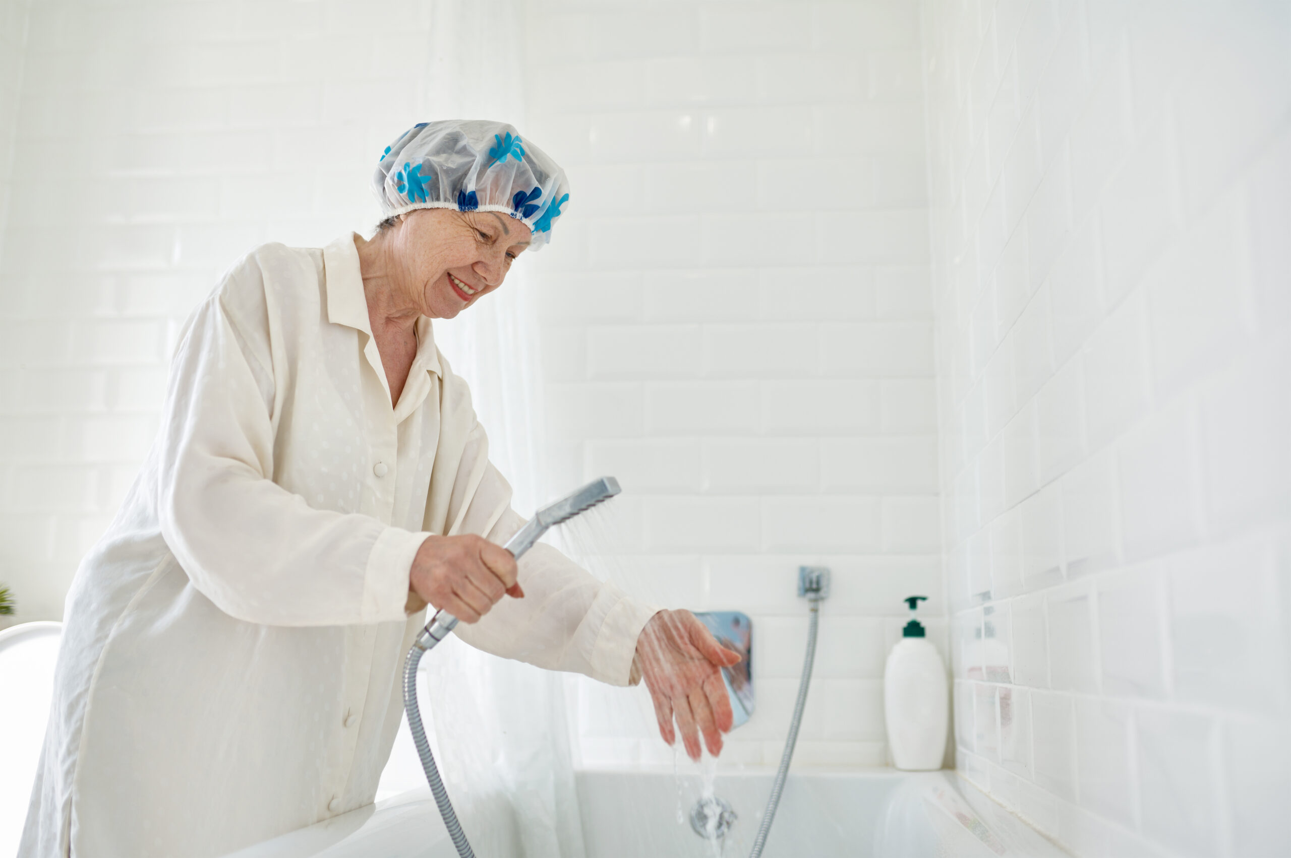 Una persona anziana utilizza uno spruzzino in una vasca da bagno, dimostrando l'accessibilità e la comodità delle soluzioni pensate per la loro sicurezza e autonomia nel bagno.